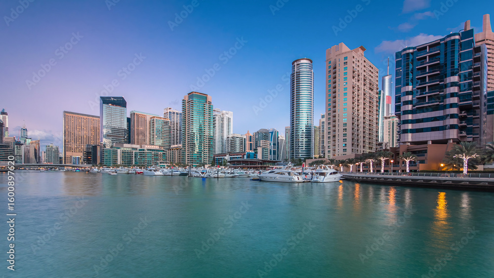 Fototapeta premium Dubai Marina towers and yachts reflected in water of canal in Dubai day to night timelapse