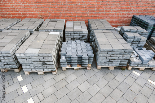 Konzept Baustelle Vorbereitung, Lieferung, Pause oder Baustopp: Unterschiedliche Pflastersteine auf Paletten gestapelt auf einem Grundstück vor einer roten Klinkerwand – selektiver Fokus, Textfreiraum