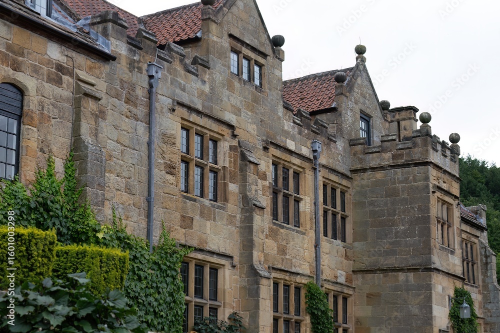 Fototapeta premium Historic stone building with tiled roof and ivy base; architectural grace softened by nature’s quiet reclaiming in Mount Grace Priory - East Harlsey - North Yorkshire - UK