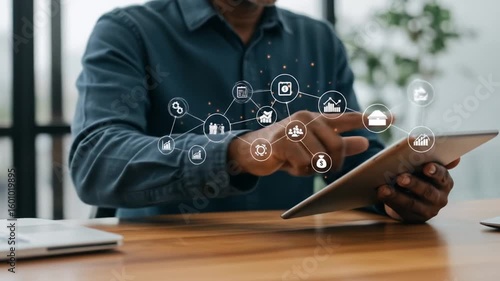 A person uses a tablet on a wooden desk, digital icons overlay the image, suggesting financial and business data visualization