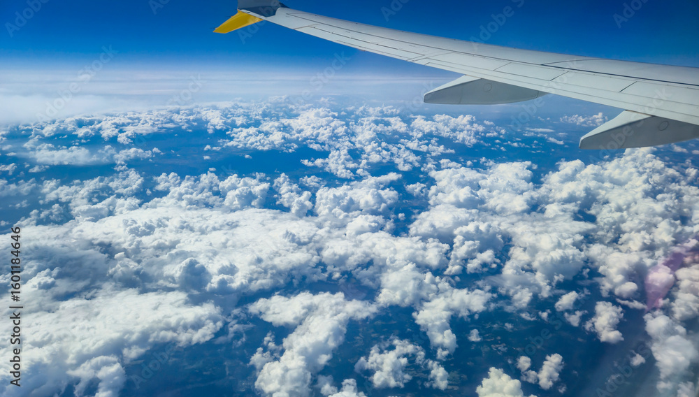Fototapeta premium Airplane wing above fluffy clouds on a sunny day. The view captures the vastness of the sky and the beauty of the cloud formations, perfect for travel-themed projects.