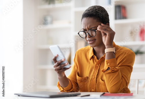 Slika na platnu Confused pretty millennial black woman in casual outfit looking at cell phone sc