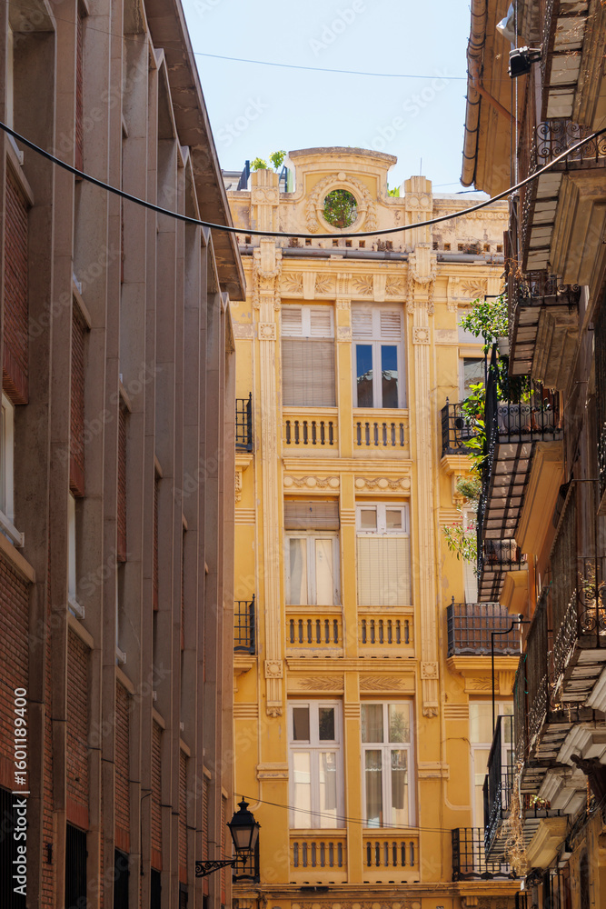 Fototapeta premium Narrow street view showcasing a beautiful yellow building surrounded by modern architecture in Valencia, Spain, reflecting the city's rich architectural heritage.