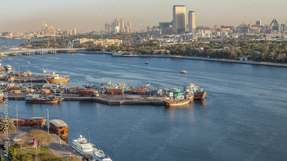 Fototapeta premium Dubai creek landscape timelapse with boats and ship in port and modern buildings in the background during sunset