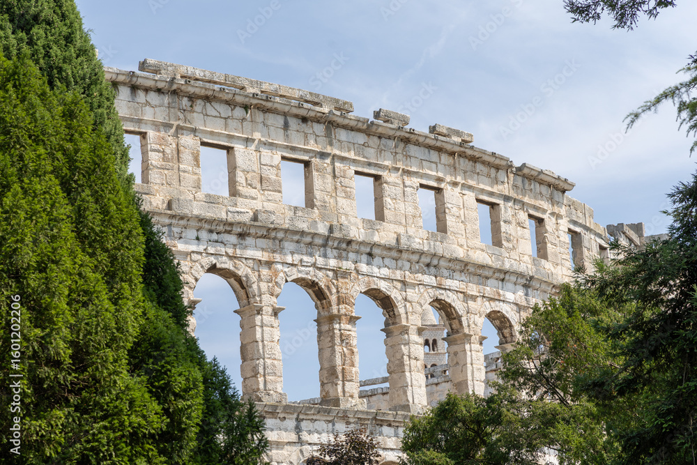 Obraz premium Ancient stone amphitheater stands majestically among lush greenery, showcasing architectural grandeur and historical significance in a serene outdoor setting