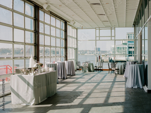 Outdoor terrace with tables set for an event beside the waterfront during a sunny day in a city