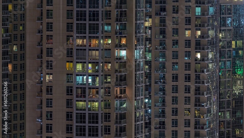 Windows of the multi-storey building with lighting inside and moving people i...