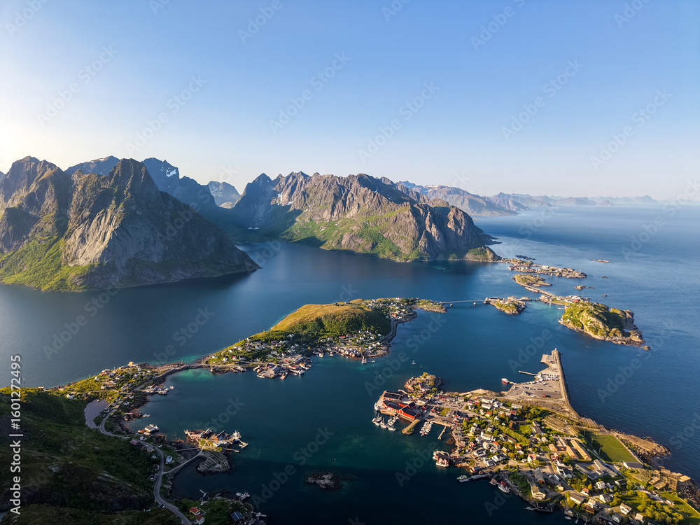 Obraz premium Panoramic aerial view of Reine village in the Lofoten Islands, Norway, surrounded by fjords, islands, and steep mountains in golden evening light.