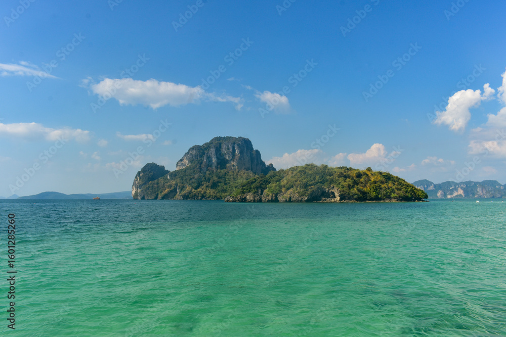 Fototapeta premium Lush green island with limestone cliffs in turquoise waters, under a clear blue sky, Krabi, Thailand.