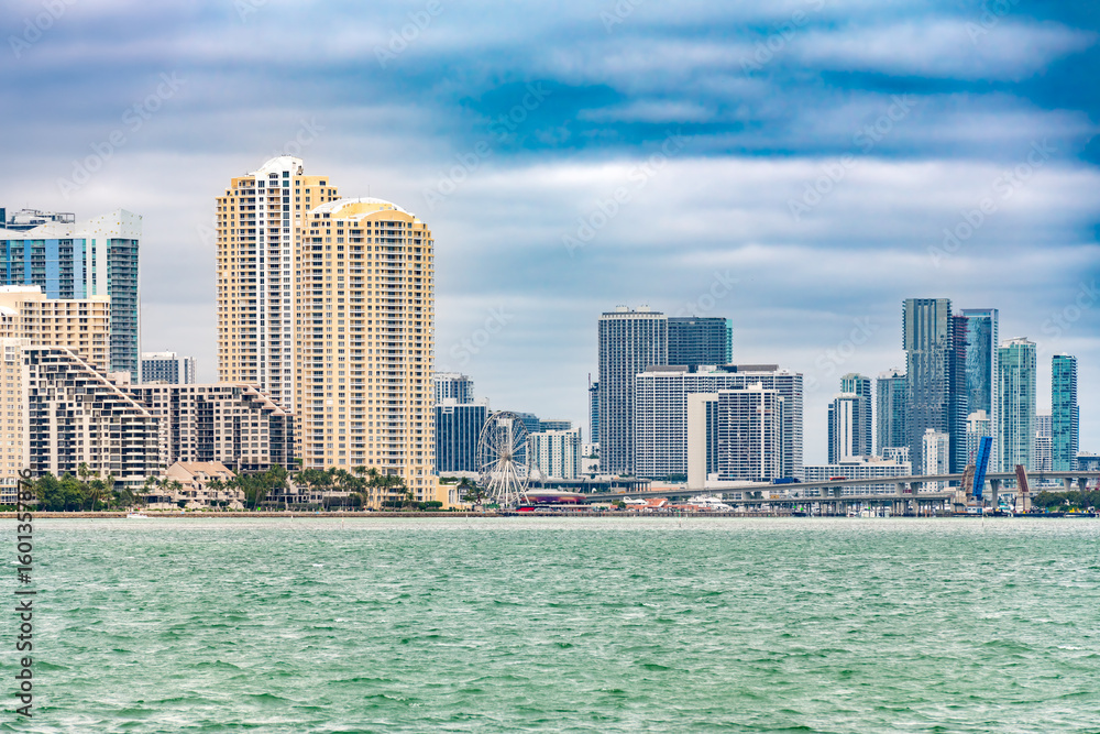 Obraz premium Downtown Miami and Brickell skyline, featuring Port Boulevard and the Skyviews Miami Wheel against a dramatic sky.