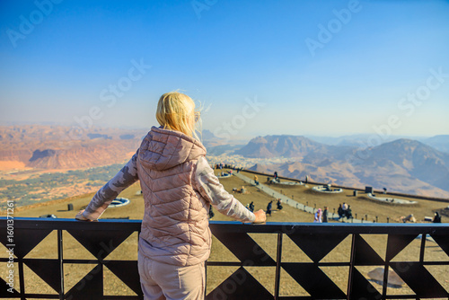 Blonde tourist admiring the breathtaking panorama of AlUla Old Town and surrounding desert landscapes from Harrat Viewpoint in Saudi Arabia