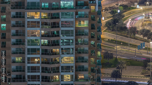 Rows of glowing windows with people in apartment building at night.
