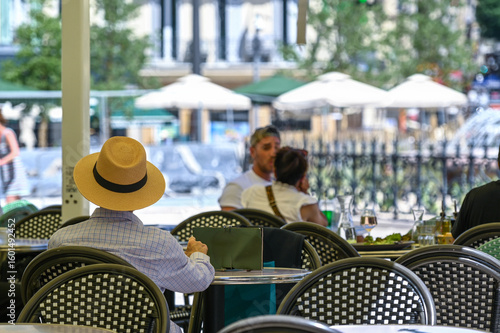 Marseille, France : Relaxed outdoor lunch in a French café. Man with straw hat sitting at table, summer sunlight, Mediterranean lifestyle, Castellane, Marseille, France