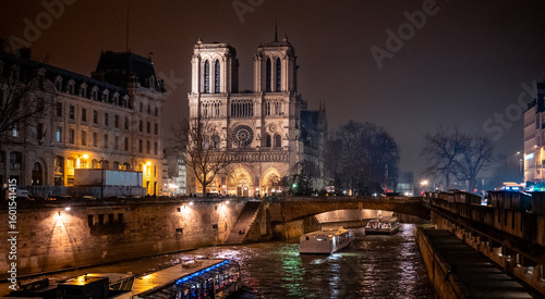 Photography Notre-Dame de Paris illuminated at night with boats cruising on the Seine river, winter cityscape and reflections