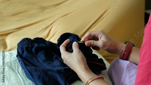 Caring mother repairing her child’s trousers by hand, focusing on sewing trouser legs.