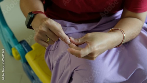A woman's hands are tying a knot of thread to prepare to sew pants.