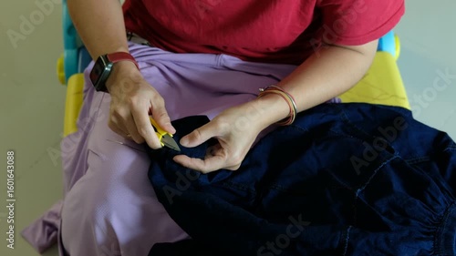 Caring mother repairing her child’s trousers by hand, focusing on sewing trouser legs.
