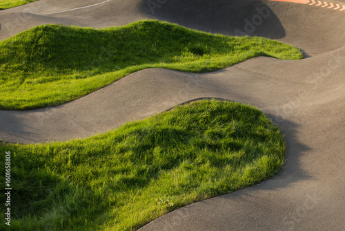 Modern pump track with grass-covered islands, creating abstract wavy landscape in evening light. Outdoor sport track detail, green urban design and active lifestyle concept