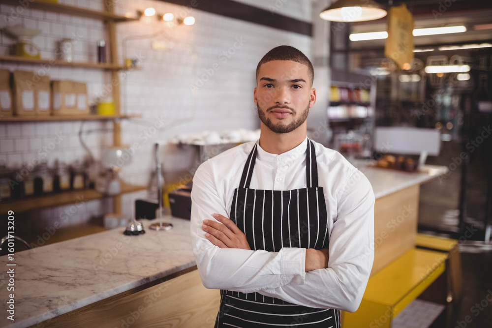 Fototapeta premium Man in twenties standing behind marble counter with service bell wearing apron at coffee shop