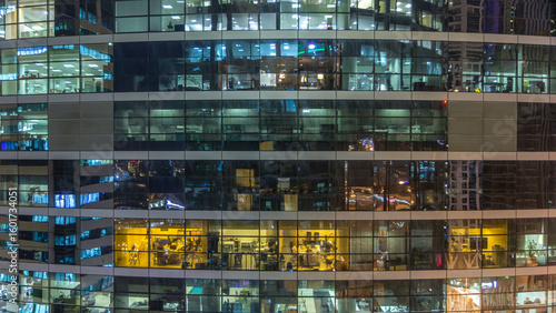 Glowing windows in multistory modern glass and metal office building light up...