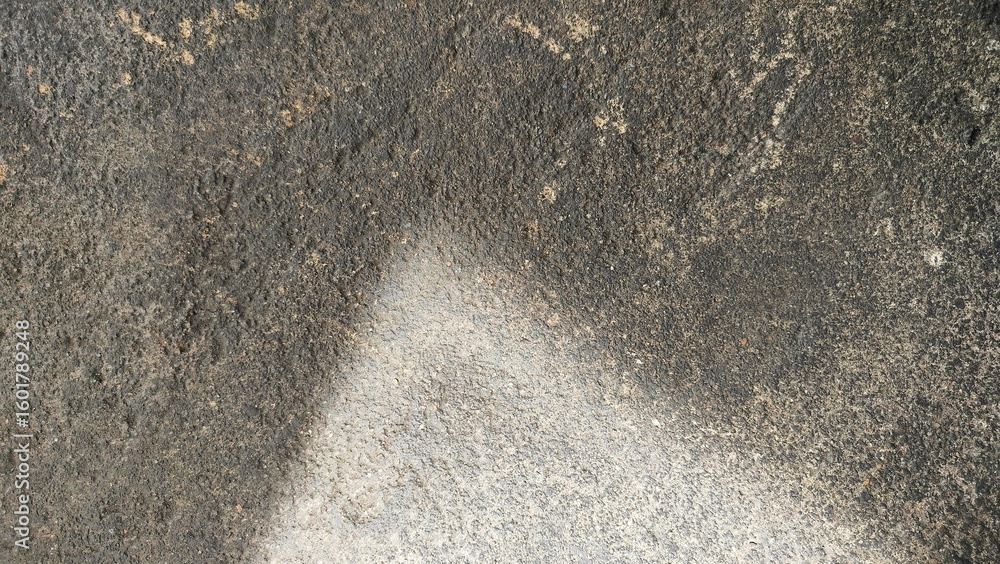 Obraz premium a close-up view of a rough, textured surface—likely an aged concrete or asphalt pavement. The surface is weathered, with uneven coloration, featuring dark patches light discoloration, and gritty mater