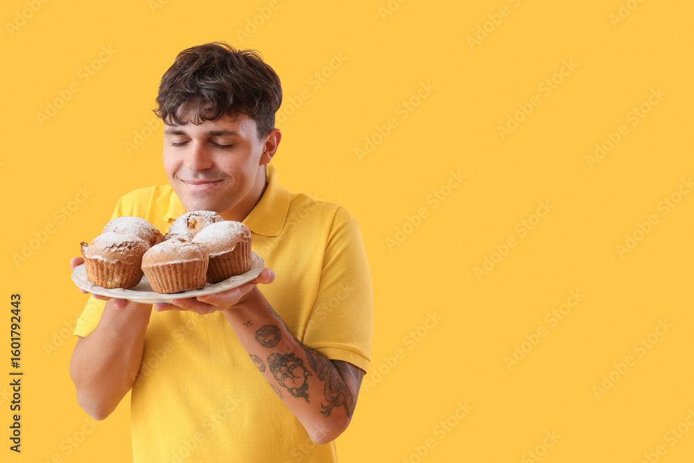 Young man with tasty muffins on yellow background Young man with tasty muffins on yellow background