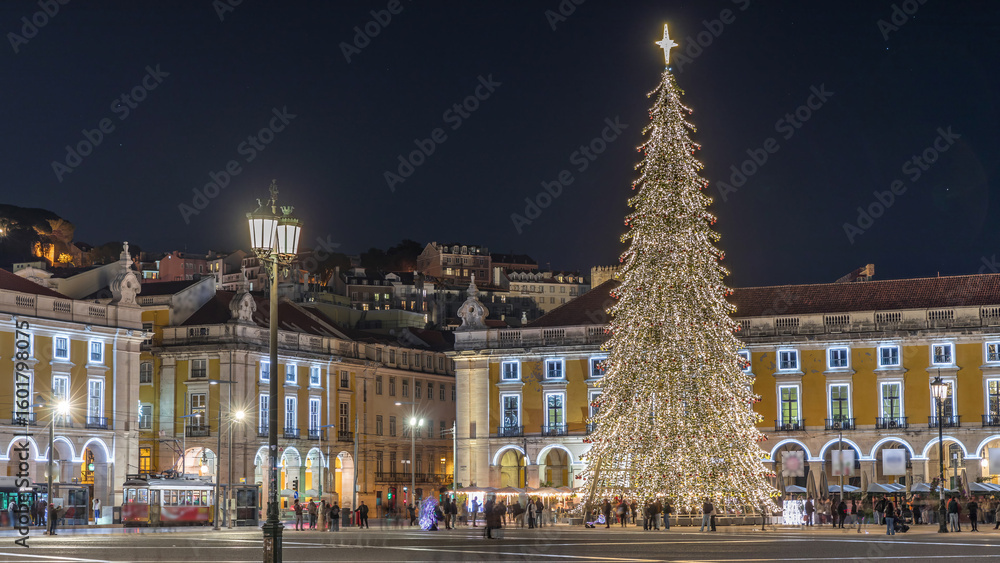 Naklejka premium Commerce Square in Lisbon illuminated at Christmas hyperlapse, with a towering tree and crowds celebrating at night. Portugal