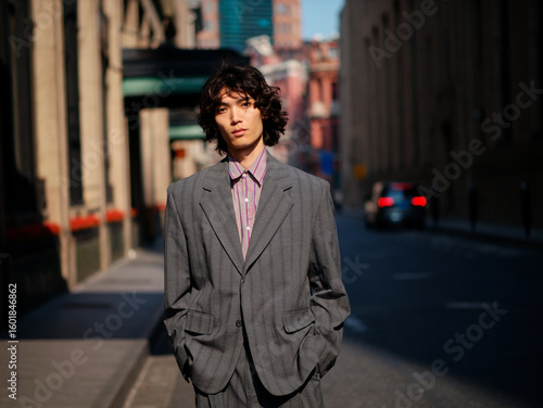 Portrait of handsome Chinese young man wearing gray suit posing in the street, young guy with black curly hair with urban background. Male fashion, cool Asian young man lifestyle.