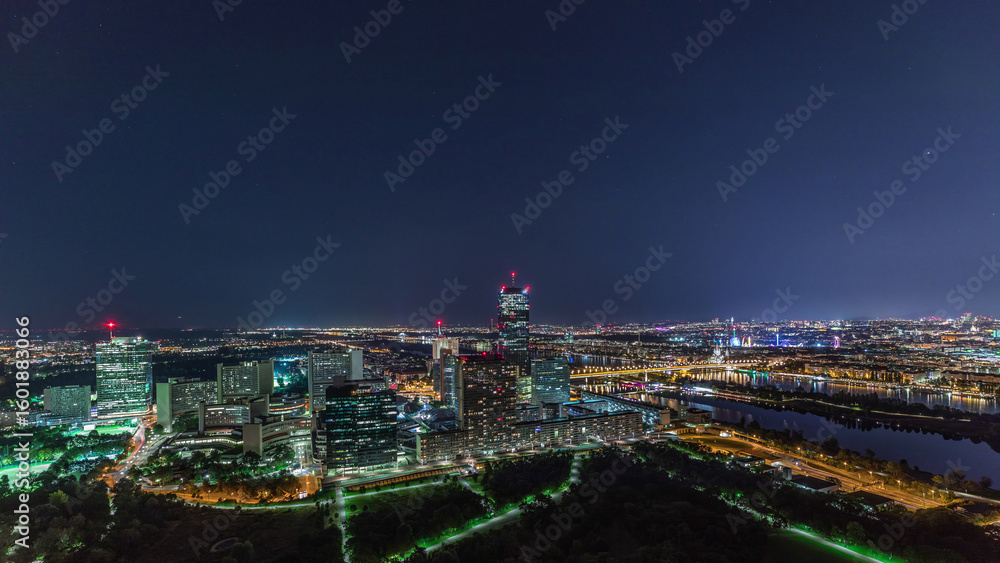 Obraz premium Aerial panoramic view over Vienna city with skyscrapers, historic buildings and a riverside promenade night timelapse in Austria.