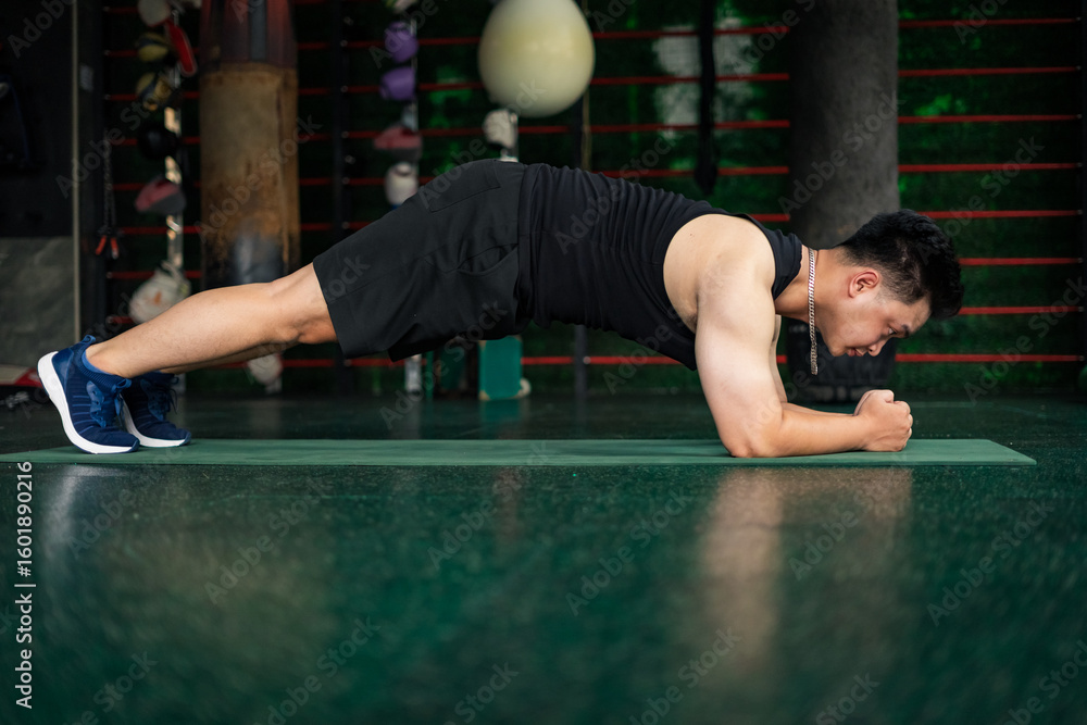 Fototapeta premium Young Asian man performs plank exercise in gym during training session for strength and endurance building