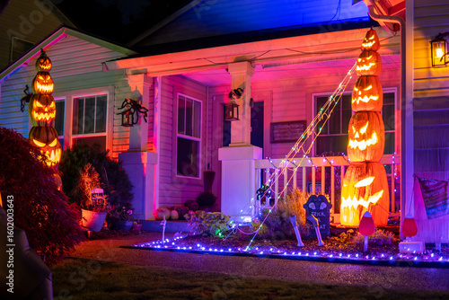 Halloween house decorations with orange lights, glow garlands and pyramid of pumpkins. Illuminated night decor