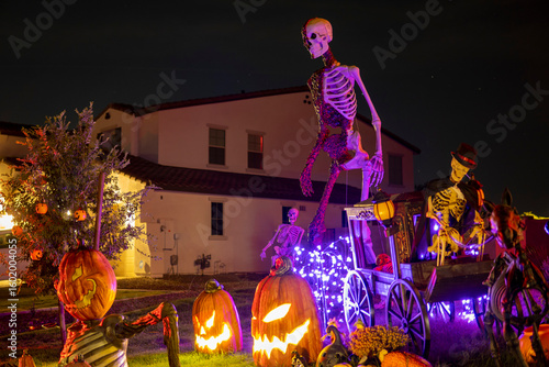 Illuminated night Halloween house outdoor decorations with garlands, skeleton and scary Jack-o-lantern emerges from the ground next to other pumpkins
