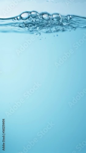 ultra-realistic slow motion macro video of a pristine, pure blue water wave undulating upwards with shimmering air bubbles, filling the vertical frame. Bright studio lighting creates stunning