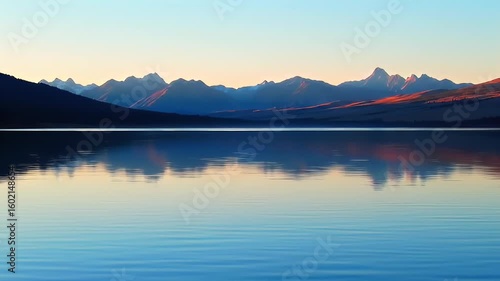 Mountain range reflecting on calm, still lake during warm dawn or dusk light