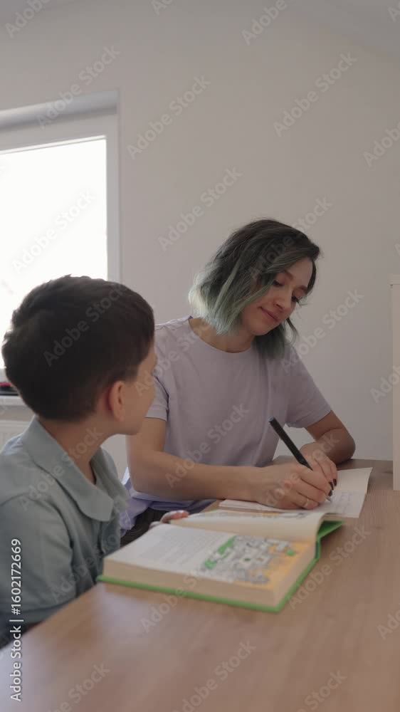 A young mother patiently assists her son with his homework, fostering a loving bond of learning and support at the kitchen table. A young mother patiently assists her son with his homework, fostering a loving bond of learning and support at the kitchen table.
