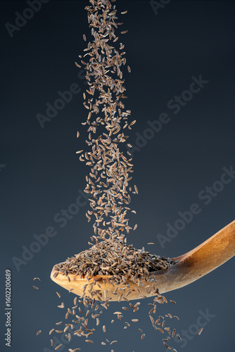 Brown cumin seeds fall from above onto a wooden spoon, ideal for aromatic seasoning and exotic recipe preparation concepts.