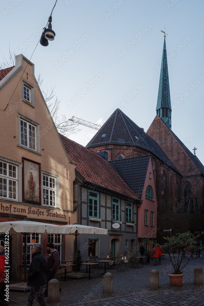 Obraz premium A street scene in the historic Schnoor Quarter (Schnoorviertel) of Bremen, Germany, with the St. Johann Church in the background.