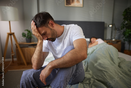 Εκτύπωση καμβά A man sits at the edge of the bed, distressed and thoughtful, while a woman lies under the covers, indicating tension in their relationship at night