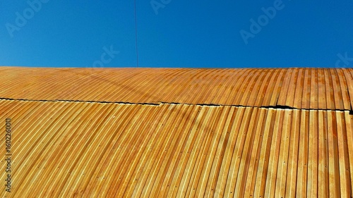 A close-up of a weathered wooden roof with horizontal planks under a clear blue sky, showcasing natural texture and rustic charm
