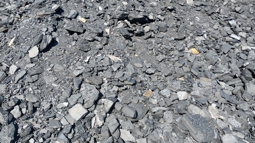 A close-up view of a rough, rocky surface covered in gray gravel and small stones, with scattered patches of green moss or grass growing between the cracks