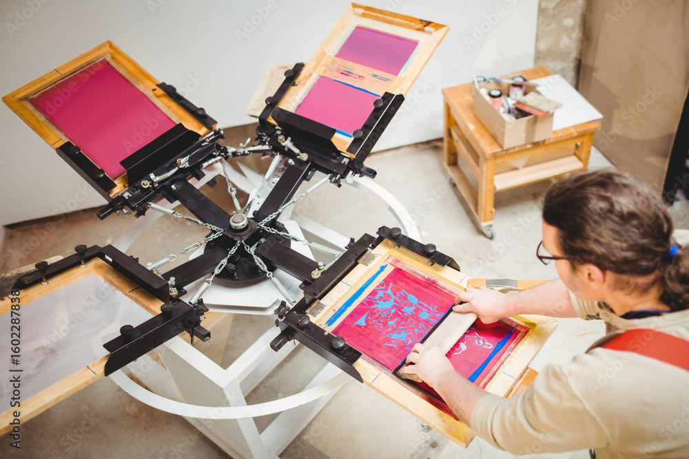 Fototapeta premium Screen printing press rotating on carousel in studio dispensing inks onto screens and supply cart