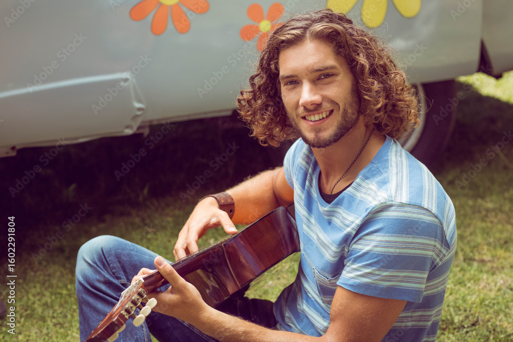 Fototapeta premium acoustic guitar is resting on green grass in front of retro camper van, with flower graphics