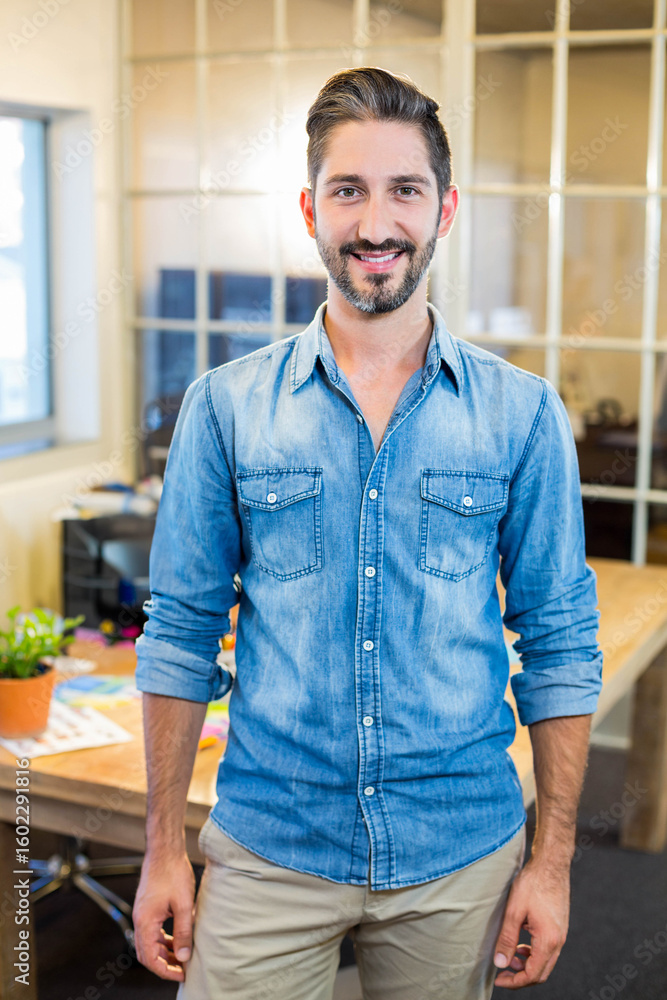 Fototapeta premium Man standing at wooden desk in modern office with plant, scattered papers and glass partition