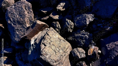A close-up of large, rugged rocks with rough textures and dark shadows, illuminated by natural light, highlighting their uneven surfaces and natural formations