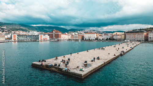 Wallpaper Mural Aerial view of a long concrete pier stretching into the turquoise sea, bustling with people under a dramatic sky, Trieste, Friuli-Venezia Giulia, Italy. Torontodigital.ca