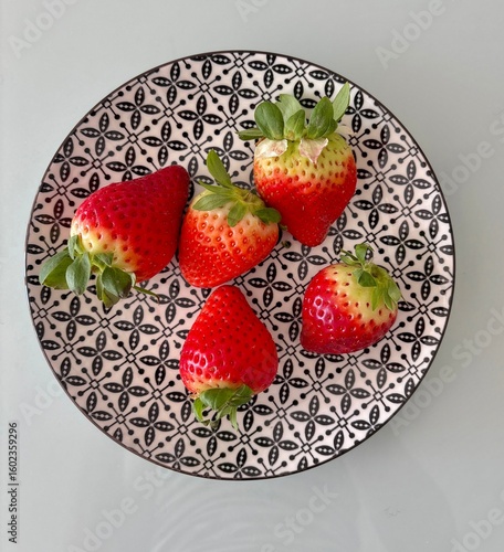Fresh ripe strawberries on a decorative black and white patterned plate. A top-down flat lay view highlighting the vibrant red color and natural texture of the fruit
