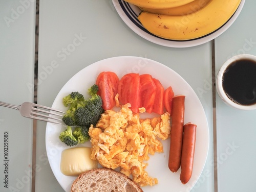 A healthy and colorful breakfast plate with scrambled eggs, sausages, vegetables, bread, cheese, and a cup of black coffee, ready to start the day