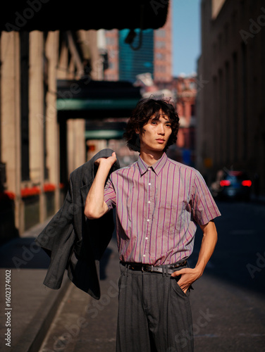 Portrait of handsome Chinese young man wearing stripe shirt posing in the street, young guy with black curly hair with urban background. Male fashion, cool Asian young man lifestyle.