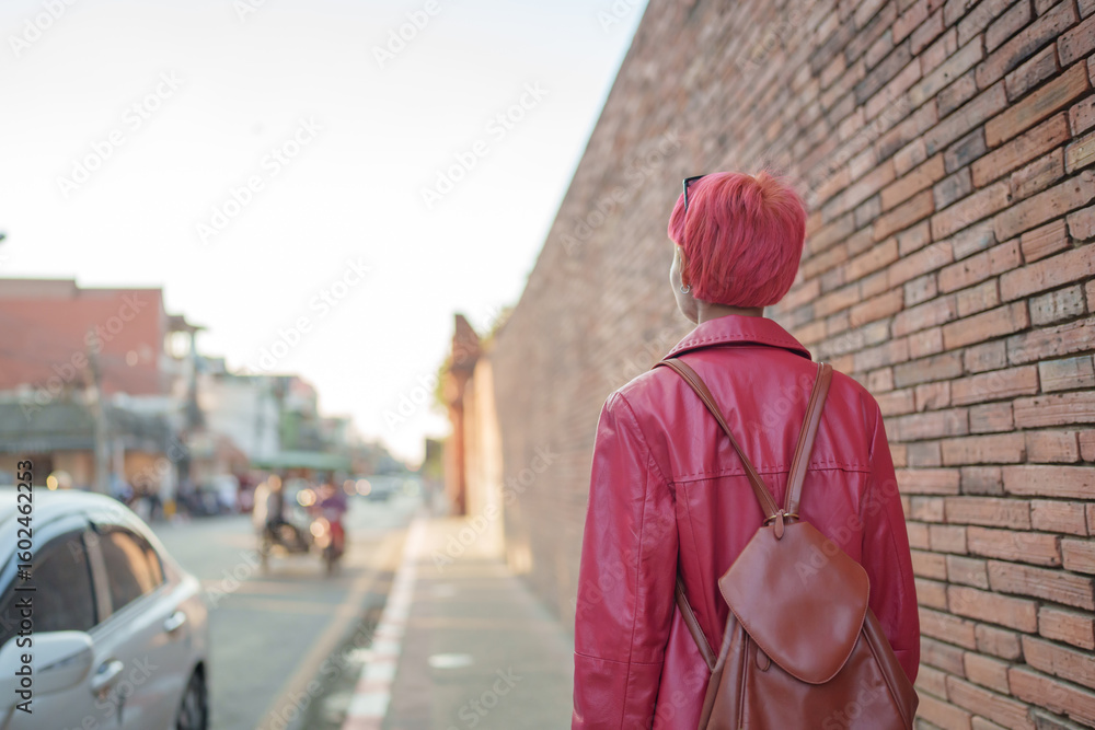 Obraz premium Gen z girl leather fashion with punk Asian woman tourist of local city Southeast Asia travel trendy pink hairstyle young female punk traveler walking around in town