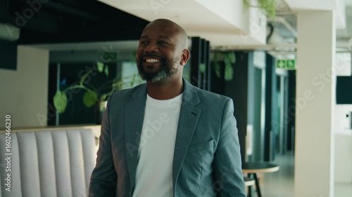 Smiling mature black businessman walking confidently through office on bright workday